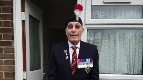 Pete Wilson in his full military uniform. He has a string of medals attached to his jacket and a cap with a red and white feather in it on his head.