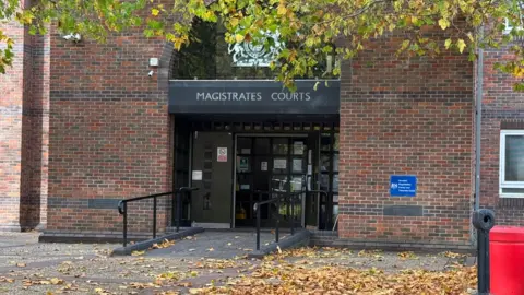 A view of the entrance of red brick building. A ramp leads up to a set of double doors. A sign above says "Magistrates Court".