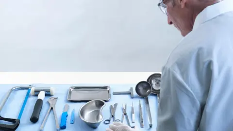 A stock image of a pathologist looking at tools needed to carry out an autopsy 