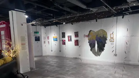 Willow's Rainbow Box Art displayed on walls as well as a knitted set of wings hanging from the roof