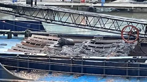 John Cameron A boat with a large object on the back of it, lying on what appears to be rows of wooden planks