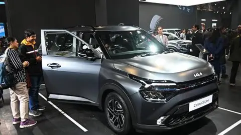 The image shows two men looking inside a matt finished black KIA Car displayed during the Bharat Mobility Global Expo 2025, ain New Delhi, India. 