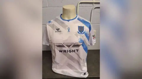 Paul Ross Ballymena United shirt which features a sky blue ribbon.