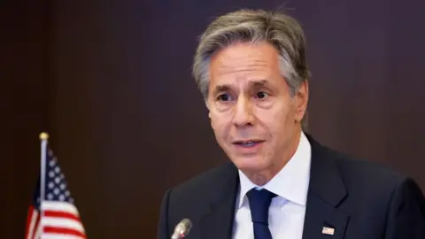 Getty Images Close up shot of Antony Blinken speaking into a microphone. He is wearing a dark blue jacket, white shirt and dark blue tie. In the back