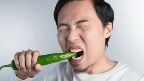 A man in pain biting a large green chilli
