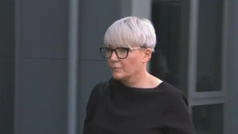 A woman with glasses and short silver hair walking outside a building