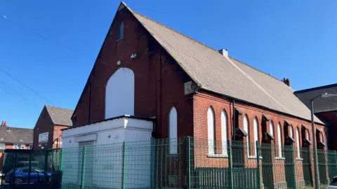 A large redbrick building with a steeply pitched tiled roof.