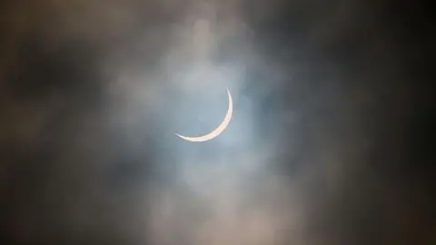 The sun is pictured during a partial solar eclipse. The sky is dark and cloudy. The sun is a thin arc in the sky. This was the partial solar eclipse seen over Glasgow in March 2015