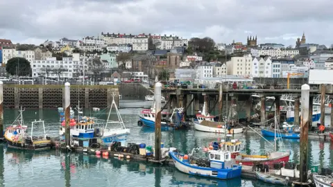 View of St Peter Port taken with the town's harbour in the foreground. Several boats of various sizes are in the marina.