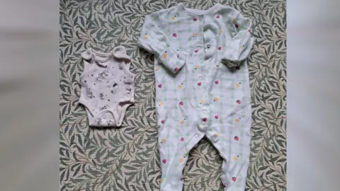 Emma Baugh / BBC Two babygro outfits placed next to each other - one small white with teddy bears on it and another green and white checked with fruits on it