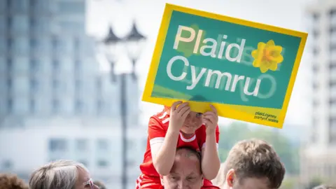 Rob Norman/Plaid Cymru A young boy holding a Plaid Cymru banner on a man's shoulders.