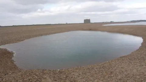 Felixstowe Coastguard Rescue Team A hole on a beach, filled with water.