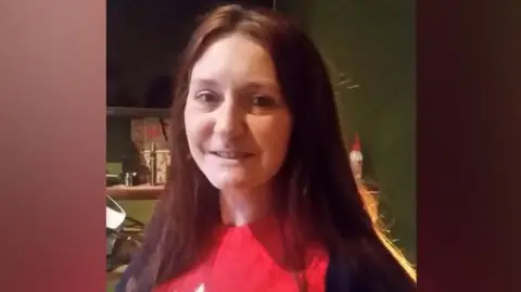 Family Photo Natalie Jones, who has long brown hair and wears a red jumper and is smiling and looking at the camera