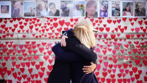 PA Media People hugging as they attend a ceremony marking the fifth anniversary of the Covid-19 pandemic at the National Covid Memorial Wall in London.