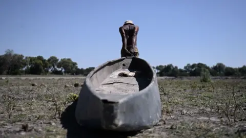 A Poller Drags A Traditional Boat Across A Dried Channel Where They Use To Use Boat Near The Nxaraga Village In The Okavango Delta On The Outskirts Of Maun