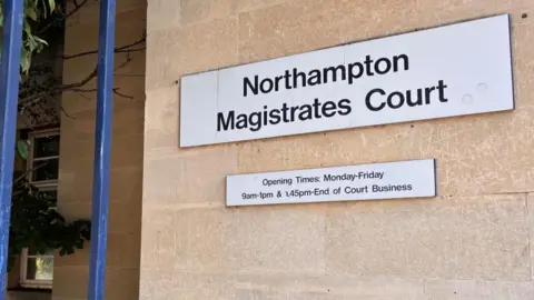 Brian Farmer/BBC Northampton Magistrates Court: a white sign, on a brown wall, saying, in black letters, "Northampton Magistrates Court". A similar sign below gives opening times.