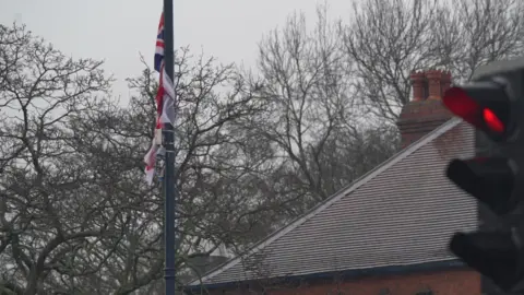 BBC A union jack is attached to a flag pole. A sloping roof can be seen on the right with a traffic light in the foreground
