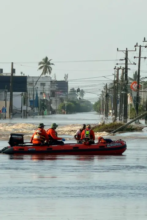 LFB Firefighters in a red RIB rescue boat with floodwater all around.