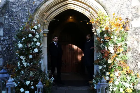 Reuters Church entrance with floral diaplays on either side and two ushers standing inside the doorway