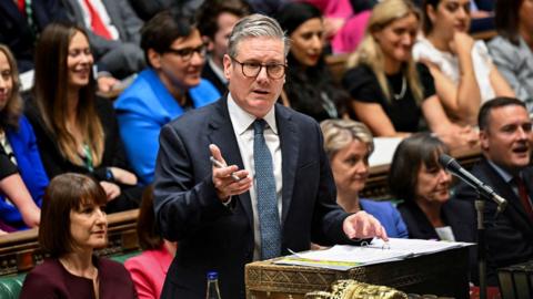 Sir Keir Starmer wearing a suit and speaking from the despatch box in the House of Commons, with Rachel Reeves sitting behind him 