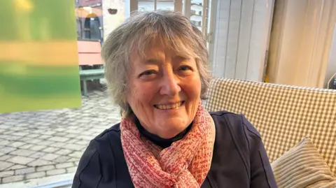 A woman with a navy blue top and red speckled scarf sitting on a chair.