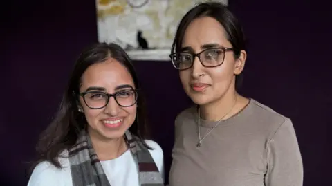 Sisters Sana and Sumiyyah stood together in a living room. 