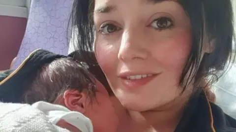 Niki Cotson cradling her newborn son while lying on a hospital bed. Both have dark hair, with Niki's being in a short bob cut.
