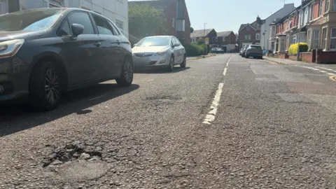 A pothole on a road with cars parked next to it