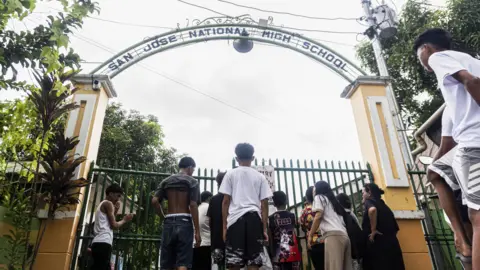 EPA A small crowd gathers at the gate of the San Jose National High School in Tacloban City after a mass shooting