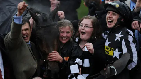 Getty Images Four people, including a jockey, gather around a bay horse following a win at Cheltenham Festival