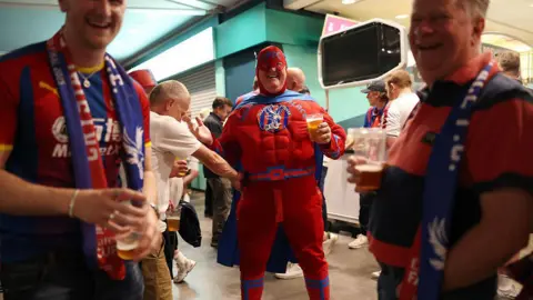 Getty Images Fans in the stadium holding beers. One wears a superhero costume