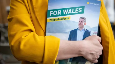 Matthew Horwood Rhun ap Iorwerth is pictured on the front page of Plaid's manifesto, which is being held by a woman in a yellow jacket. The manifesto says "for Wales" and "2026 manifesto".