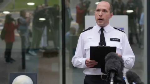 PA Media Police officer in white shirt speaks to gathered press outside police station