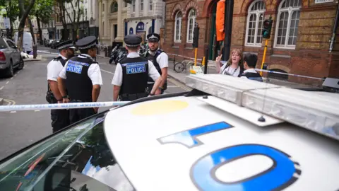 Police officers stand around a cordon with a police vehicle Endell Street in Covent Garden, central London