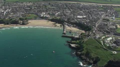 Aerial shot of a seaside town with harbour and beaches and houses stretching inland.