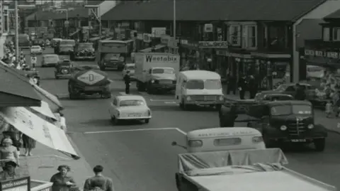 A black and white old image of the old A48 road that runs through Port Talbot from before the M4 motorway was built showing congestion as cars and lorries went slowly through the town