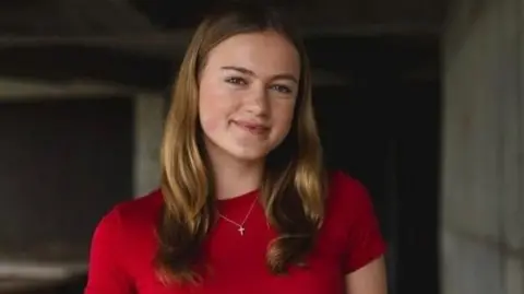 A woman with long brown hair, wearing a red top