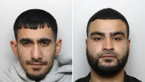 Two individual custody photographs appear side by side against a plain light background. Both people face the camera directly. The person on the left has short black hair with a straight fringe, a trimmed beard, and wears a light grey hoodie. The person on the right has short black hair, a full beard, and wears a dark top.