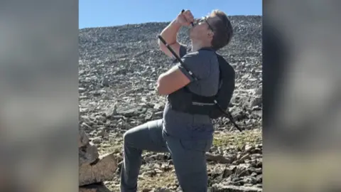 Hiker drinking from a bottle with a hiking pole piercing his torso on a rocky mountain trail