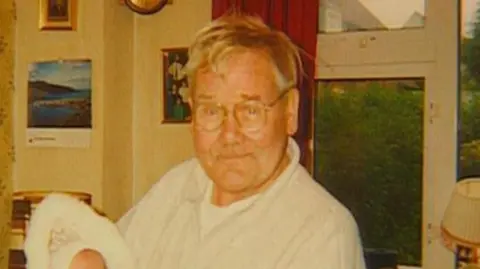 Wilson family A man aged approximately in his late 70s hold a baby that is just out of sight in his arms.