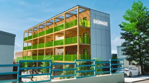 Mandy Young, Adrenaline Alley Steel and glass four-storey building, showing green balconies outside accommodation units, which are framed in yellow. There are blue railings in the foreground and industrial buildings on either side of the hotel.