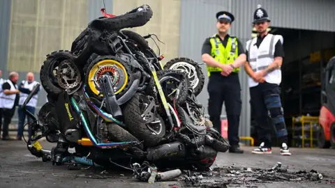 GETTY Two police officers look over a pile of seized e-scooters that have been crushed into a cube on an industrial forecourt