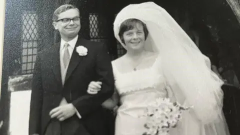 Family handout Jan and Peter Cottingham in their wedding outfits in 1966 in a black and white photograph. She has a large veil and is looking at the camera, while her husband is smiling and looking off camera in a dark suit.