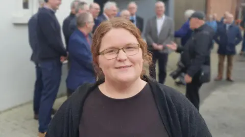 A red headed woman with glasses and a back t shirt.