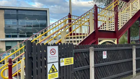 East Midlands Railway A staircase up to the footbridge behind a black fence with various warning signs attatched