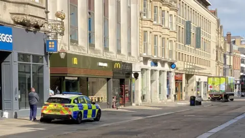 BBC A police car on an empty, cordoned off Cornmarket Street