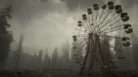 GSC Game World A screenshot from Stalker 2 shows a ferris wheel with obvious signs of decay and disrepair against a desolate backdrop of overgrown trees, a dilapidated block of flats and various ground debris. A foreboding grey mist covers the scene and specks of black ash fall from the sky.