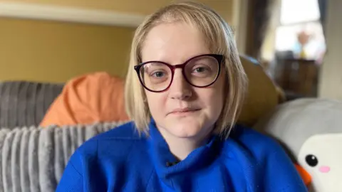 Woman with blonde hair, glasses and a blue jumper