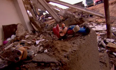 A red and blue plastic Mario toy sits on top of the bricks among a pile of other debris and rubblevcsa