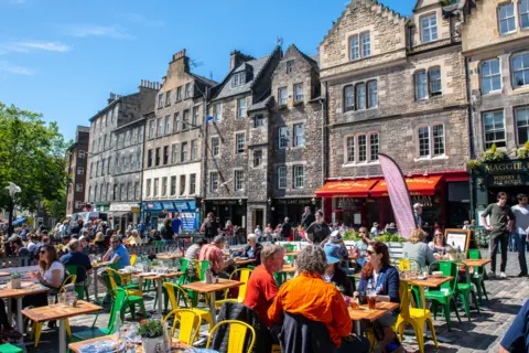 Getty Images People sitting at colourful tables and chairs in the centre of the Grassmarket.